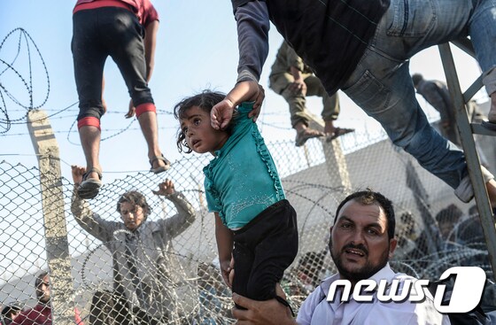 전쟁을 피해 도망온 시리아 난민이 6월 14일 터키 동남부 접경지역인 샨리우르파 주 아차칼레 인근에서 터키 영토로 들어가기 위해 자신의 아이를 국경장벽 위로 들어 올리고 있다. ⓒ AFP=뉴스1
