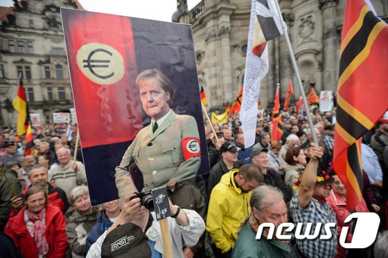 독일의 반 이슬람 극우단체 '유럽의 이슬람화에 반대하는 애국적 유럽인들'(PEGIDA·페기다)가 지난해 6월 동부 드레스덴에서 나치 제복을 입은 앙겔라 메르켈 독일 총리의 합성 사진을 들고 시위를 하고 있다. ⓒ AFP=뉴스1