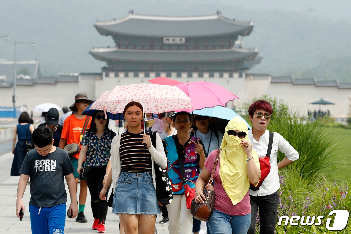 14일 서울 광화문 광장에서 옷으로 얼굴을 꽁꽁가리거나 양산을 쓴 외국인 관광객들이 걸어가고 있다.. 2019.7.14/뉴스1 ⓒ News1 안은나 기자
