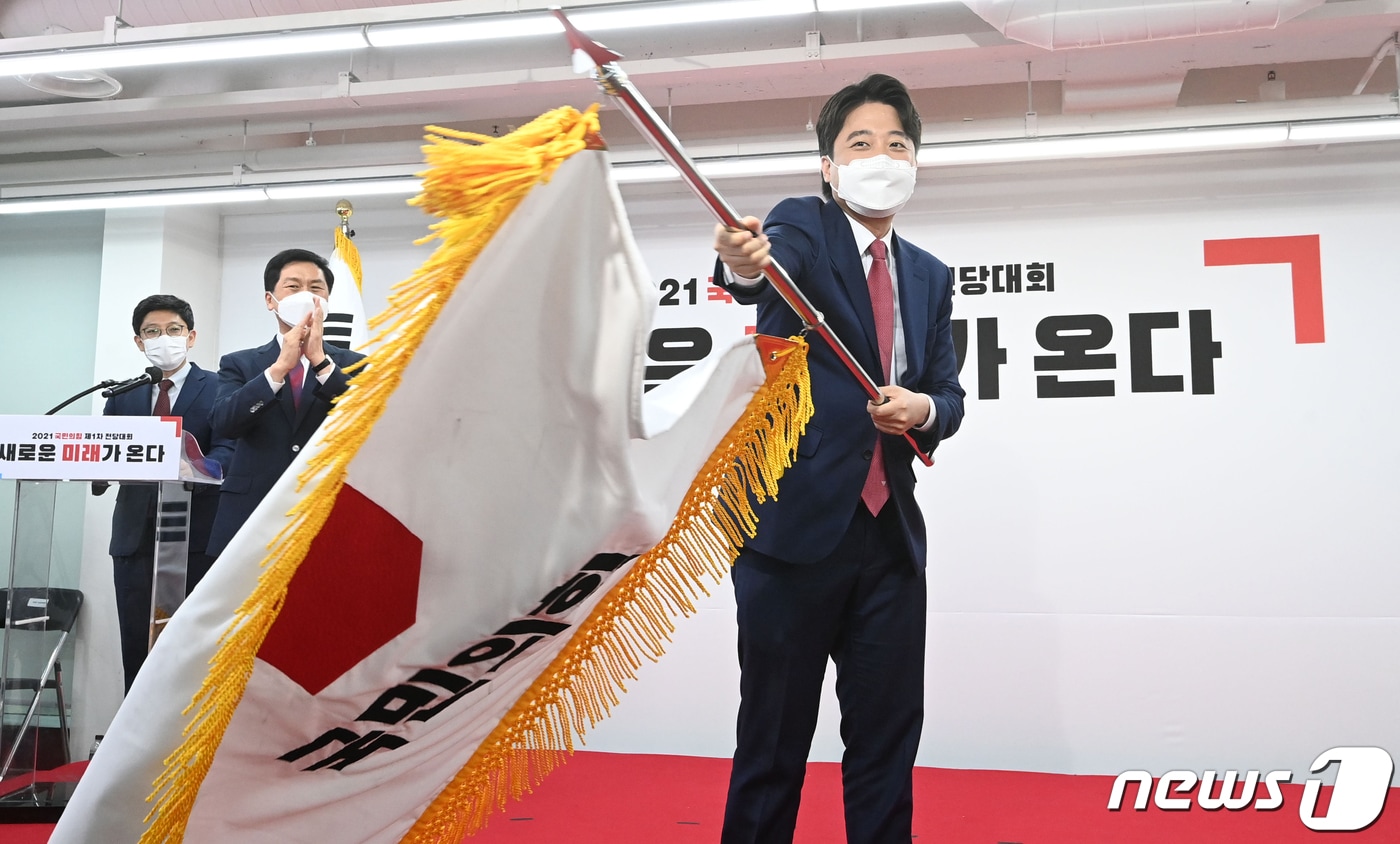 이준석 국민의힘 신임 대표가 11일 오전 서울 영등포구 국민의힘 당사에서 열린 전당대회에서 당기를 흔들고 있다. '30대·0선'의 이 대표는 역대급 전당대회 흥행을 주도한 끝에 헌정사상 최초의 30대 보수정당 대표에 올랐다. 2021.6.11/뉴스1 ⓒ News1 오대일 기자