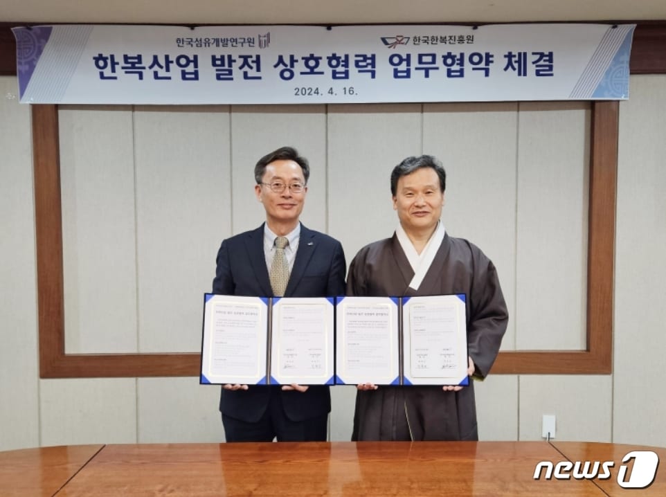 호요승 한국섬유개발연구원장(왼쪽)과 박후근 한국한복진흥원장이 한복산업분야 상호 협력과 발전을 위한 업무협약을 체결한 뒤 협약서를 펼쳐 보이고 있다.(섬유개발연구원 제공)