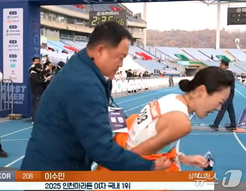 지난 23일 인천 송도에서 열린 &#39;2025 인천국제마라톤&#39; 여자 국내부 1위 이수민 선수&#40;2시간 35분 41초&#41;가 결승선을 통과한 직후 다가가던 김완기 감독의 목에 심판 비표가 걸려있었다.&#40;KBS 유튜브 캡처, 재판매 및 DB금지&#41;