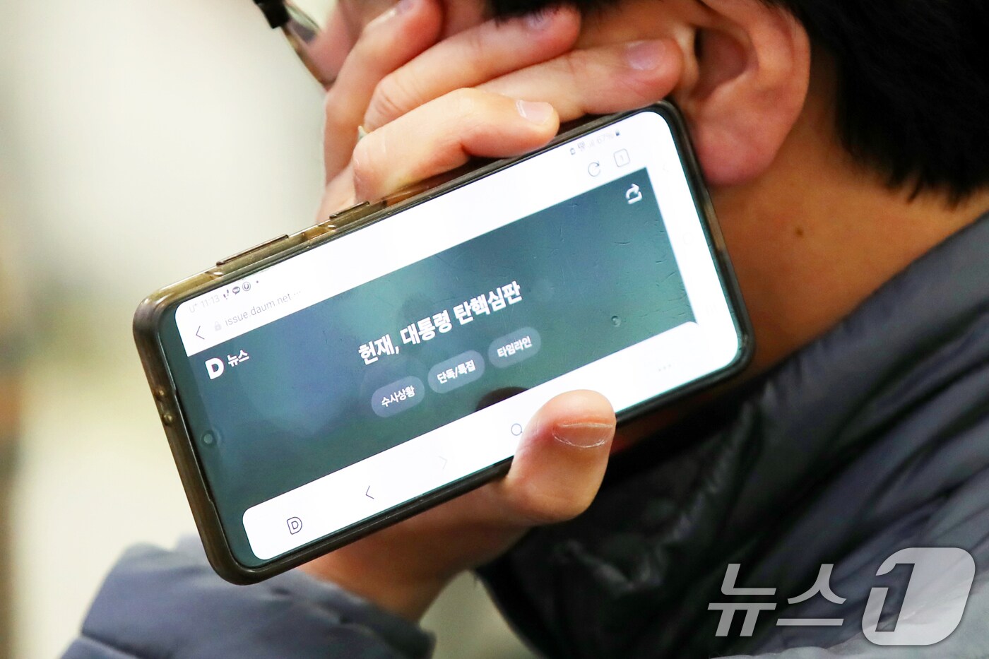 4일 오전 제주국제공항 국내선 출발장에서 윤석열 대통령 탄핵심판 생중계를 보는 관광객이 탄핵심판 뉴스 화면이 켜진 휴대전화를 들고 있다. 2025.4.4/뉴스1 ⓒ News1 오현지 기자