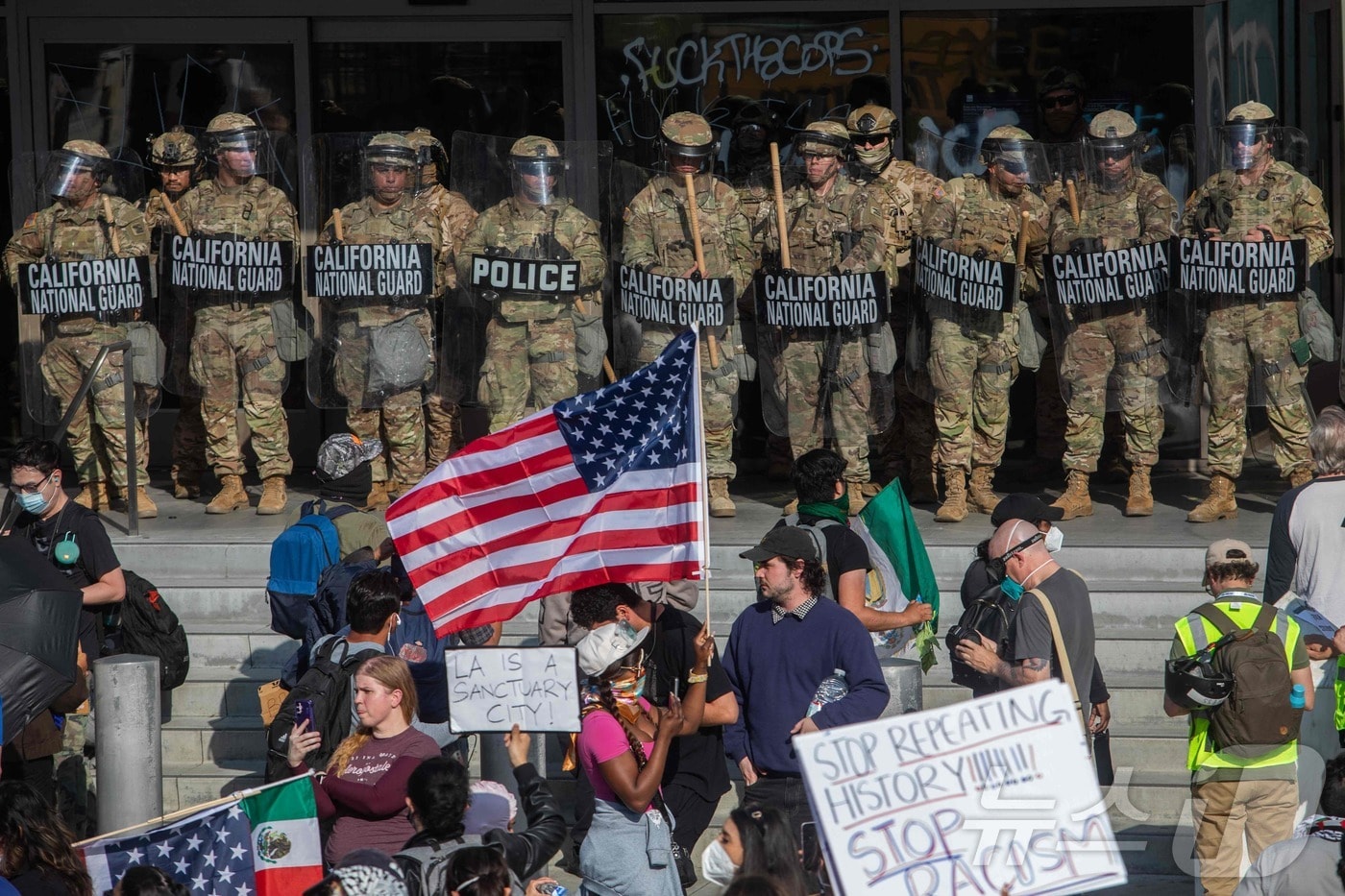 2025년 6월 9일 로스앤젤레스에서 연방 이민 작전에 반대하는 시위대가 연방 건물 밖에서 경비를 서고 있는 캘리포니아 주방위군 대원들을 향해 피켓과 깃발을 들고 있다. ⓒ AFP=뉴스1 ⓒ News1 신기림 기자