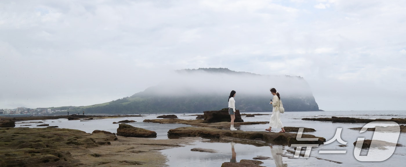 제주 서귀포시 성산읍 광치기해변에서 관광객들이 해무 낀 성산일출봉을 배경으로 사진을 찍고 있다. 2025.6.19/뉴스1 ⓒ News1 오현지 기자