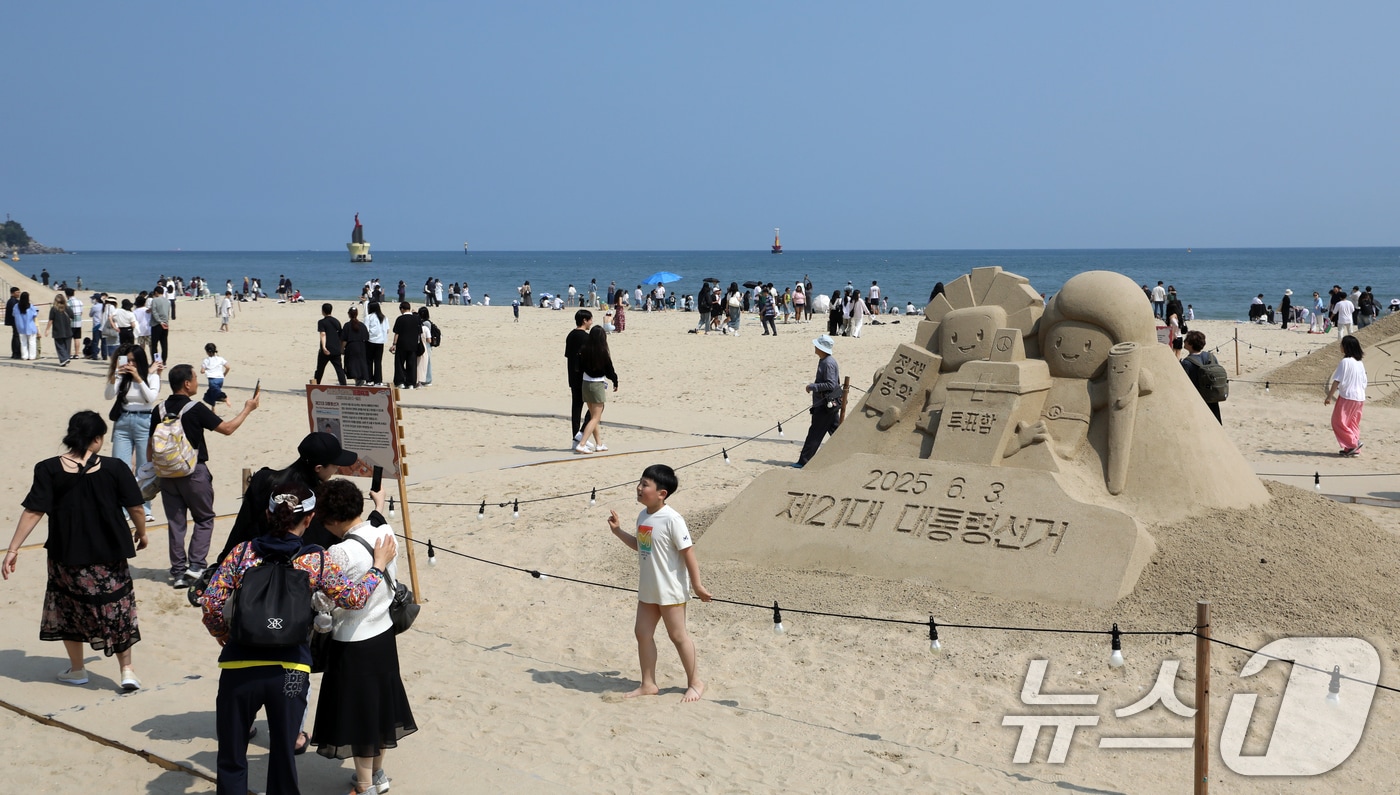 제21대 대통령 선거일이자 초여름 날씨를 보인 3일 오후 부산 해운대해수욕장에 설치된 대통령 선거 홍보 모래작품 뒤로 시민, 관광객 등이 더위를 식히고 있다. 2025.6.3/뉴스1 ⓒ News1 윤일지 기자
