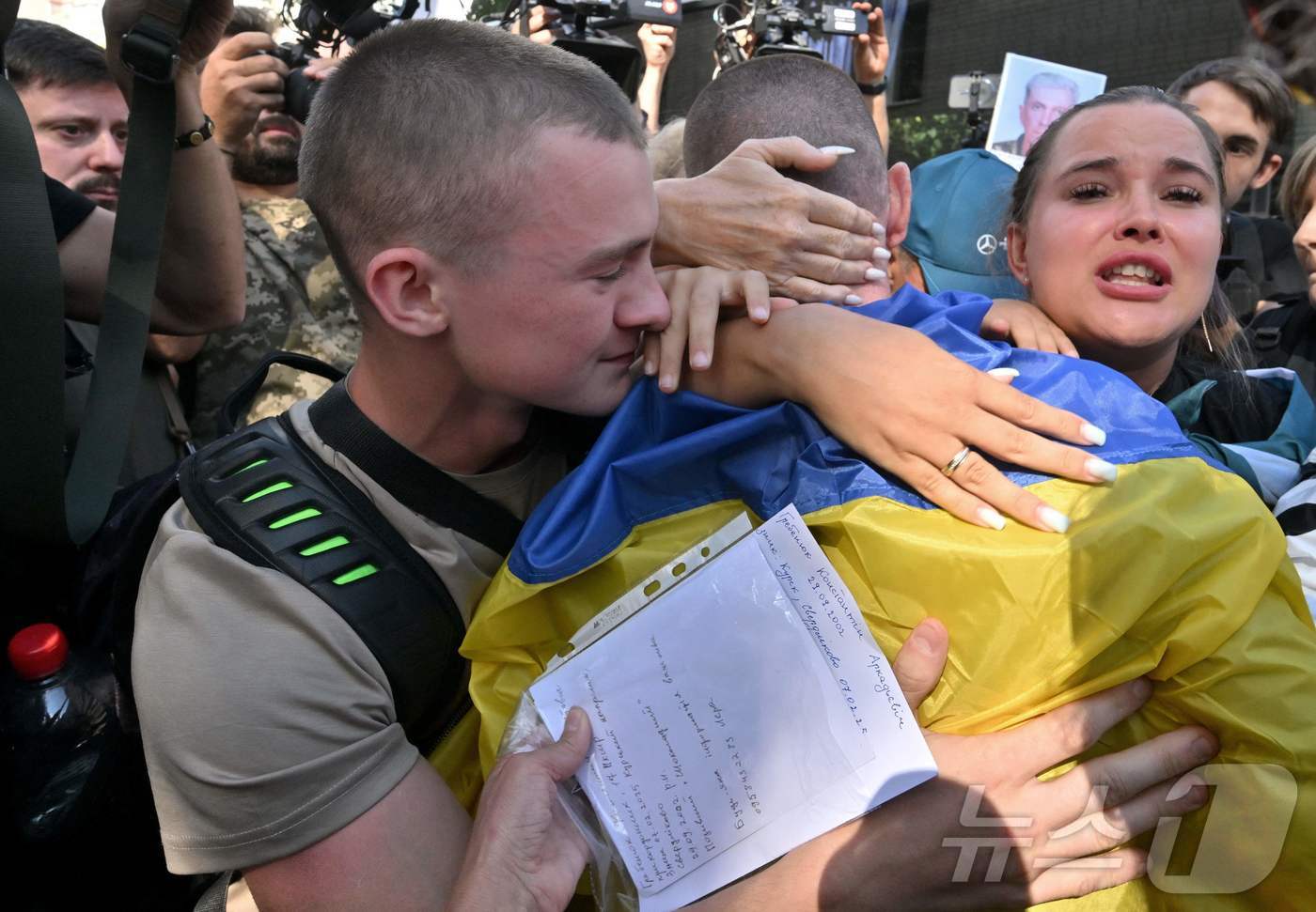 러시아에 포로로 잡혀 있다가 지난 14일 석방된 우크라이나인이 어깨에 우크라이나 국기를 두른 채로 체르니히우 지역에서 가족들과 포옹하고 있다. 2025.08.14 ⓒ AFP=뉴스1 ⓒ News1 강민경 기자