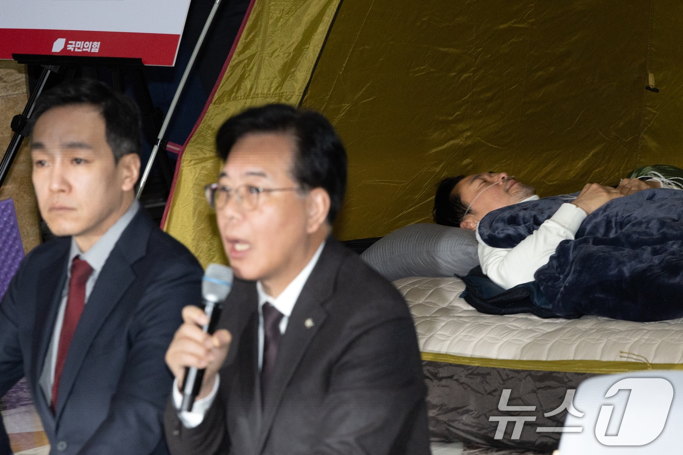 송언석 국민의힘 원내대표가 22일 서울 여의도 국회 로텐더홀에서 열린 최고위원회의에서 모두발언하는 가운데 8일째 단식 중인 장동혁 대표가 누워서 휴식을 취하고 있다. 2026.1.22/뉴스1 ⓒ News1 이승배 기자