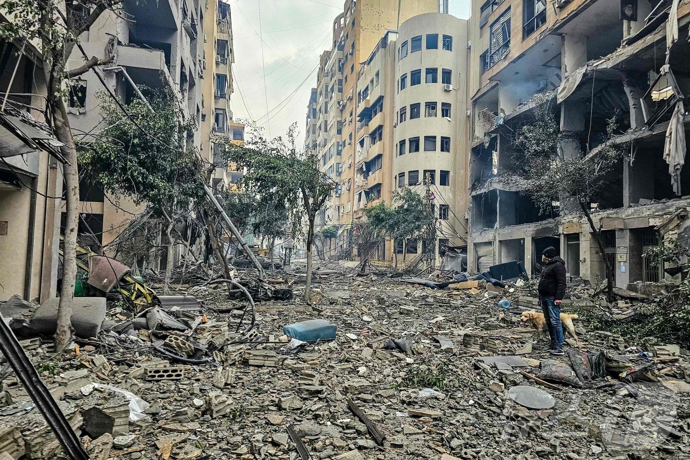 2026년 3월 15일 레바논 베이루트 남부 교외 하레트 흐레이크에서 이스라엘 공습으로 파괴된 건물 잔해 위를 한 남성과 그의 반려견이 지나가고 있다.2026.03.15. ⓒ AFP=뉴스1