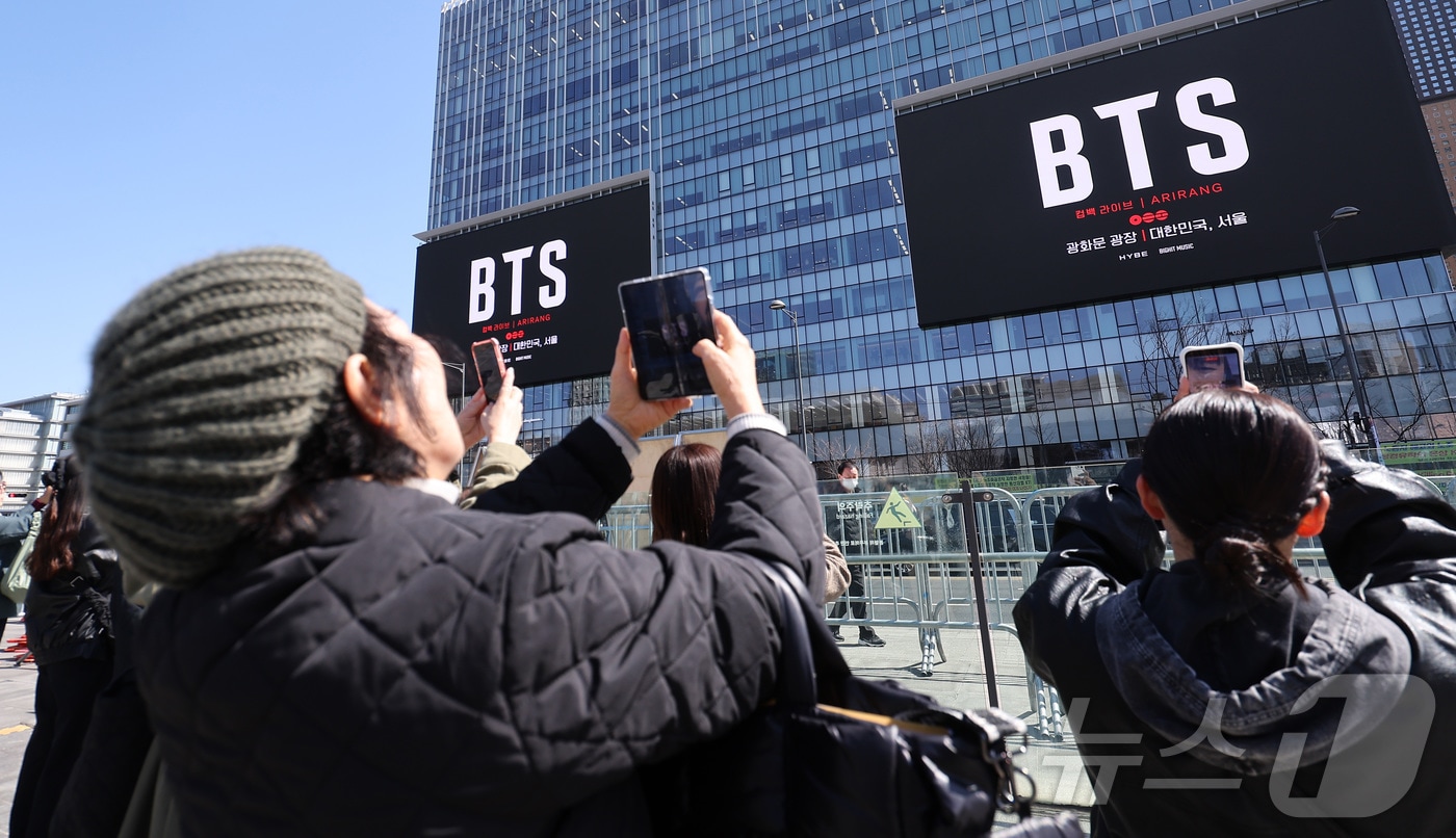 방탄소년단(BTS)의 서울 광화문광장 컴백 공연이 이틀 앞으로 다가온 19일 서울 종로구 광화문광장에서 외국인 팬들이 컴백 공연을 알리는 전광판 광고를 스마트폰으로 촬영하고 있다. 2026.3.19 ⓒ 뉴스1 김성진 기자