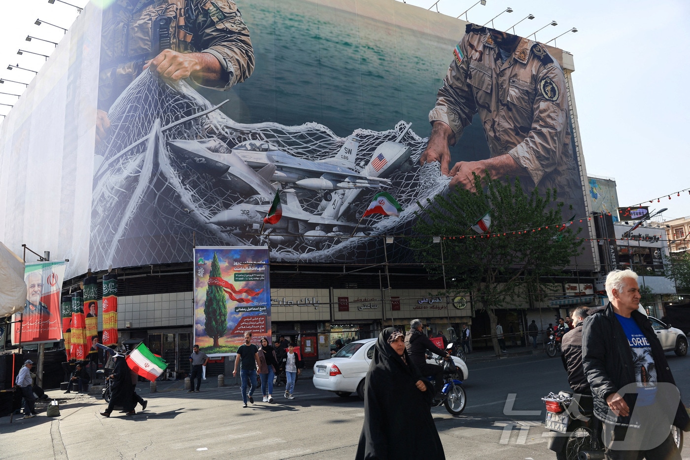 16일(현지시간) 이란 테헤란의 한 건물 앞을 시민들이 지나가고 있다. 건물 외벽에는 반미 선전물이 게시돼 있다. 2026.04.16 ⓒ 로이터=뉴스1