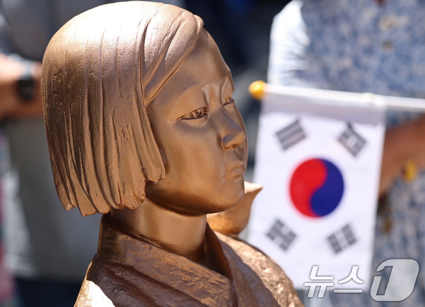 서울 종로구 옛 주한일본대사관 앞에서 열린 제14차 세계일본군 '위안부' 기림의 날 맞이 세계연대집회에서 태극기를 든 한 참가자가 평화의 소녀상 곁에 서 있다. 2026.8.12 ⓒ 뉴스1 구윤성 기자