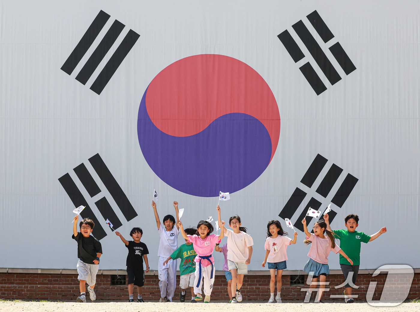 제81주년 광복절을 하루 앞둔 14일 서울 서대문구 서대문형무소역사관 대형 태극기 앞에서 어린이들이 직접 만든 태극기를 흔들며 힘차게 뛰고 있다. 2026.8.14 ⓒ 뉴스1 이호윤 기자